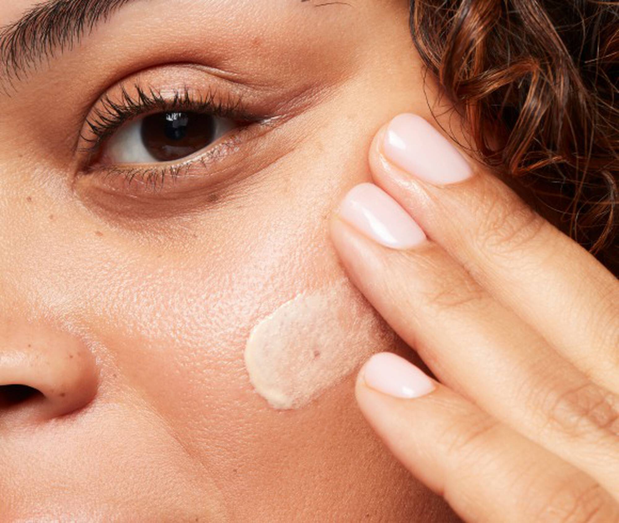 Close-up of a person applying cream to their face with a finger.