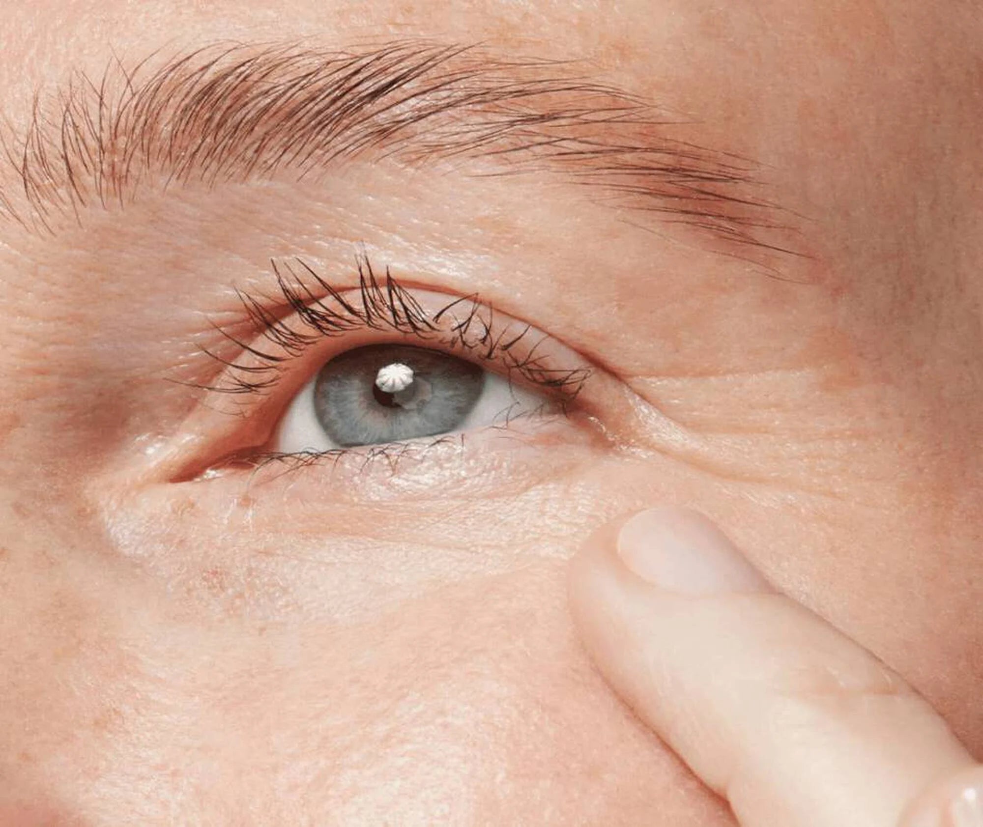 Close-up of a person's eye with a contact lens, finger on the skin around the eye.