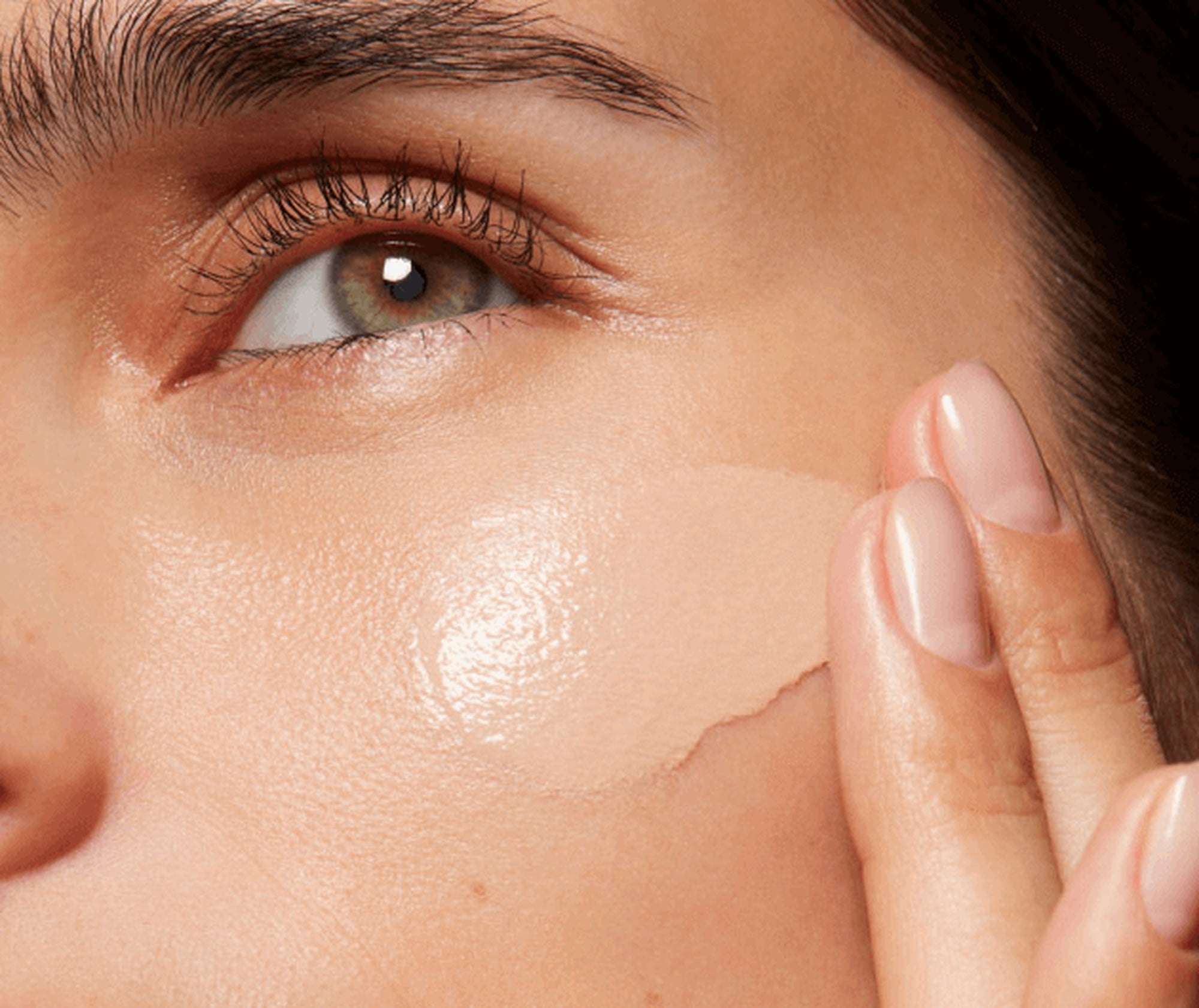 Close-up of a person applying a cosmetic product to their face.
