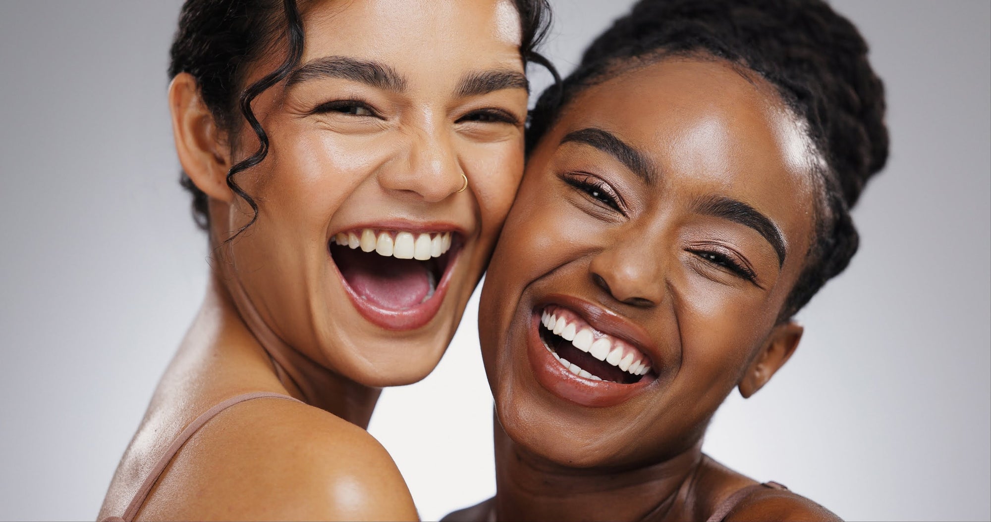 Two women laughing with a gray background