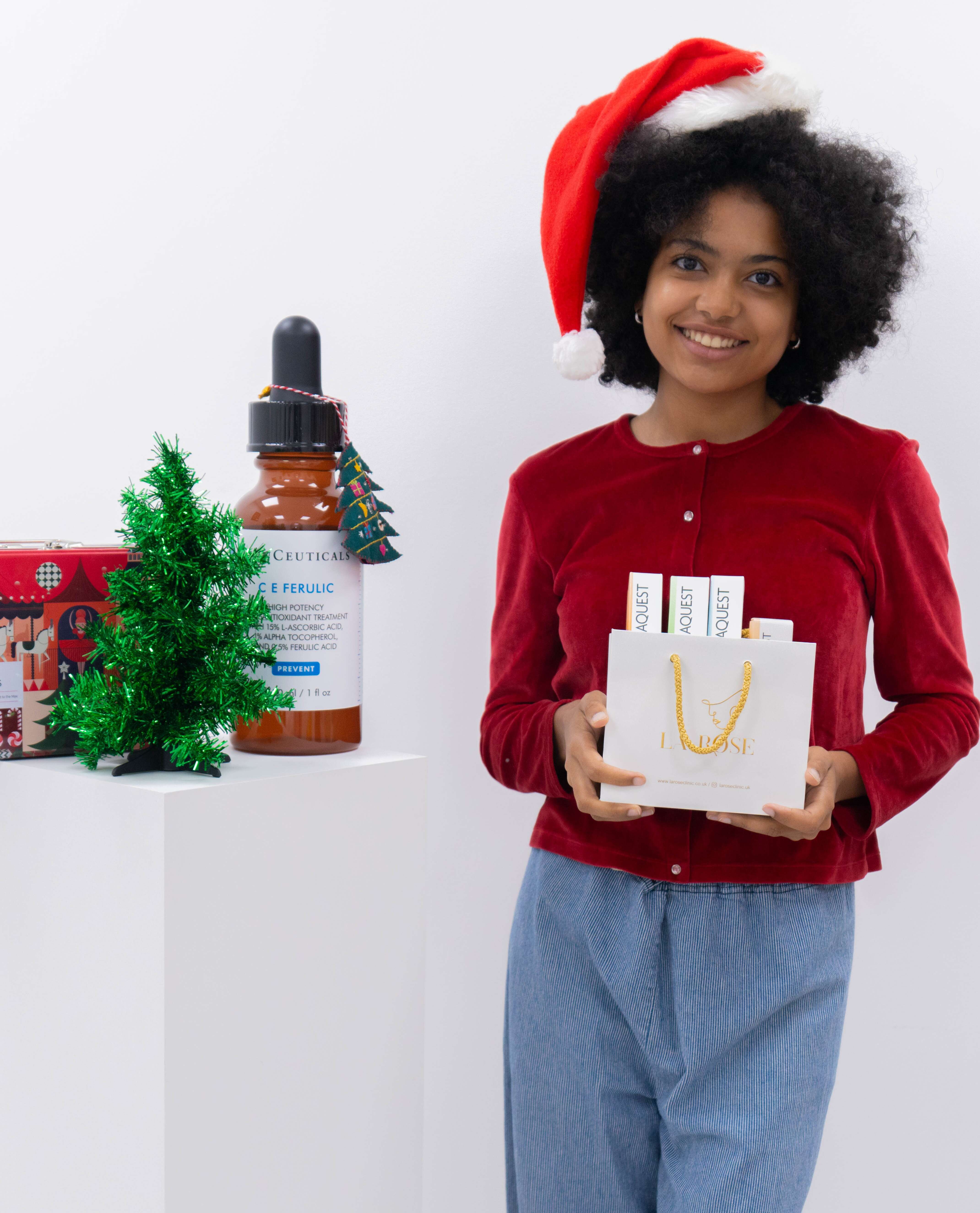 Woman in Santa hat holding a SkinCeuticals gift bag beside festive skincare display