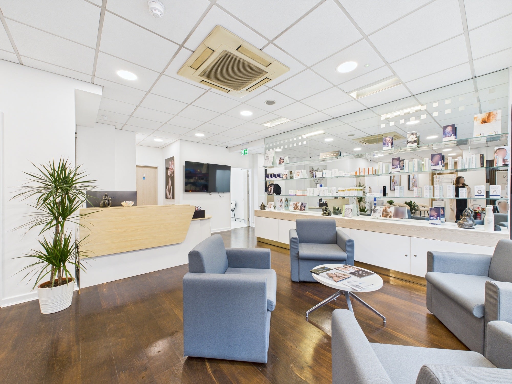 Skincare clinic waiting area with reception desk, grey chairs and product display shelves