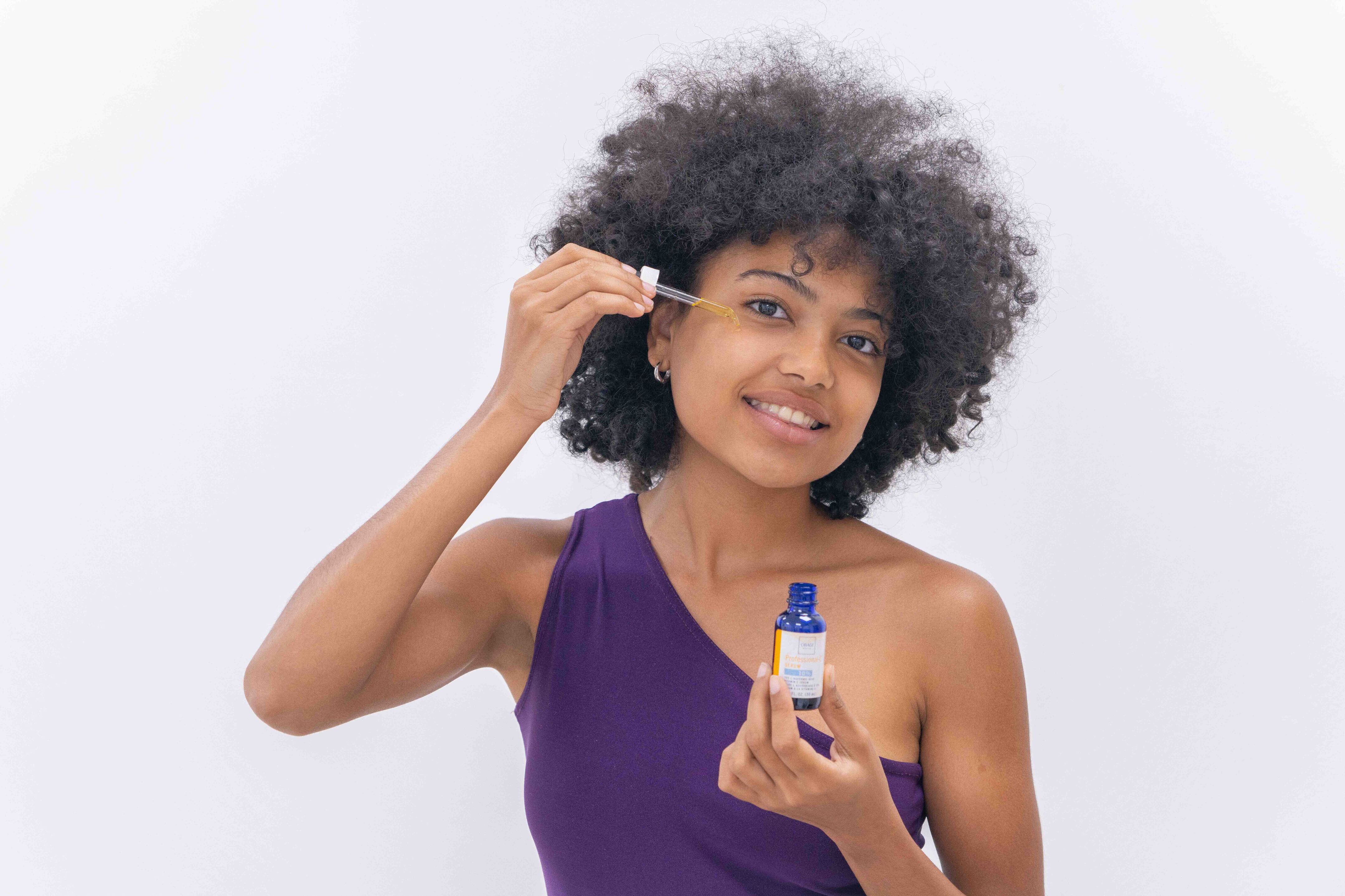 Woman applying a product to her face with a dropper bottle on a white background