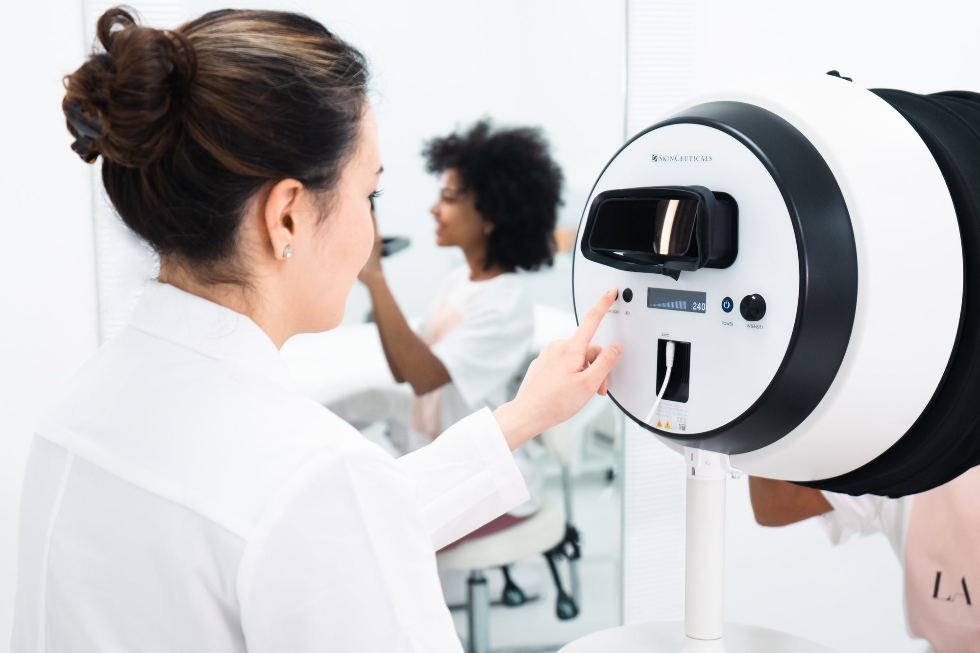 Person using a medical device in a clinical setting with another person in the background.