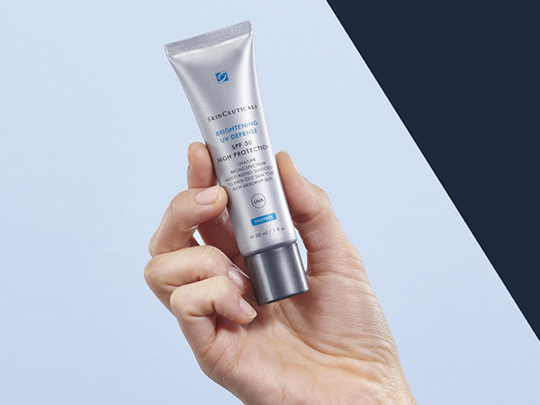 Hand holding a skincare product tube against a light blue background