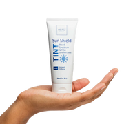 Tube of Obagi Sun Shield Tinted Broad Spectrum SPF 50 on a hand against a white background