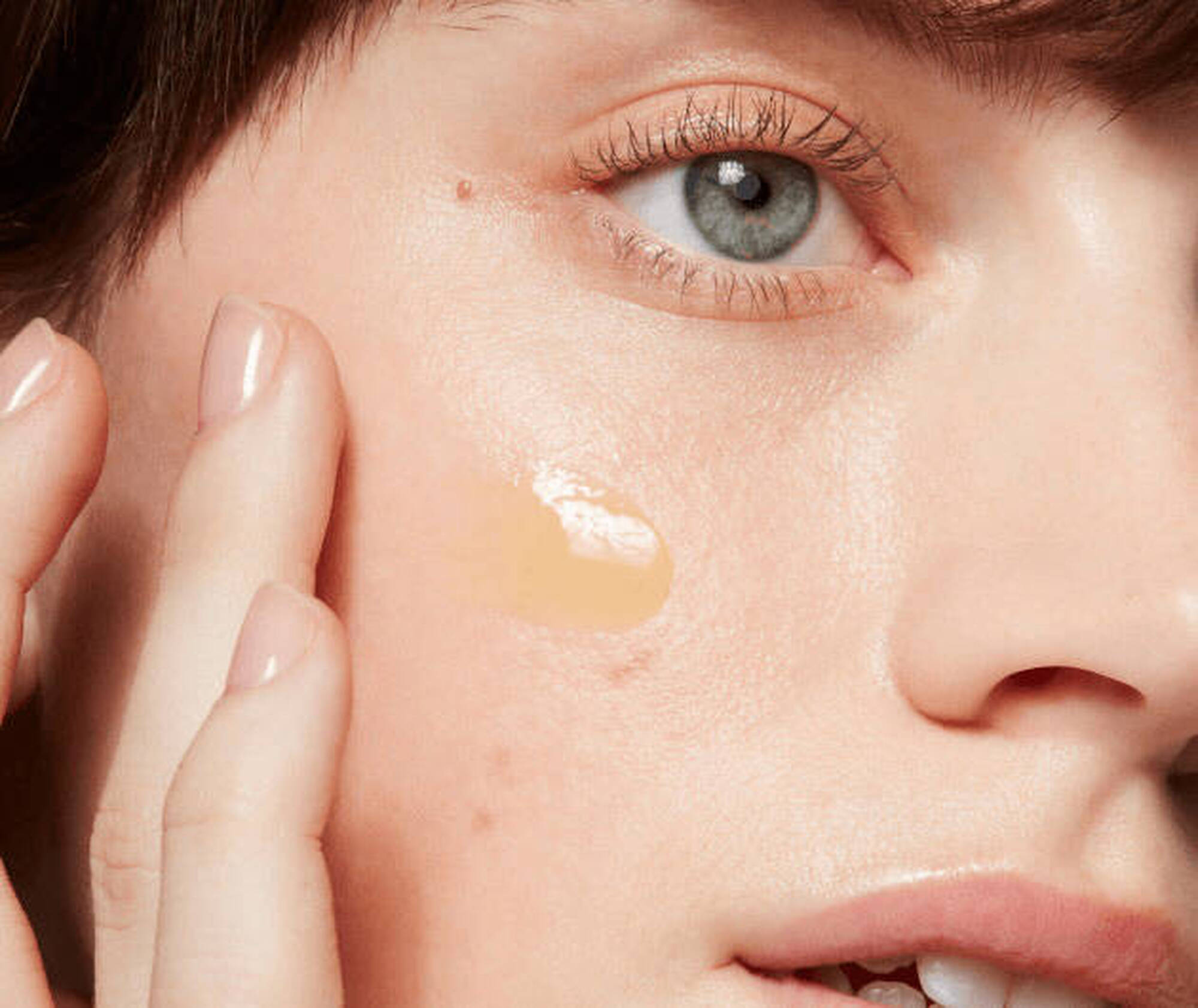 Close-up of a woman applying beige cream to her face
