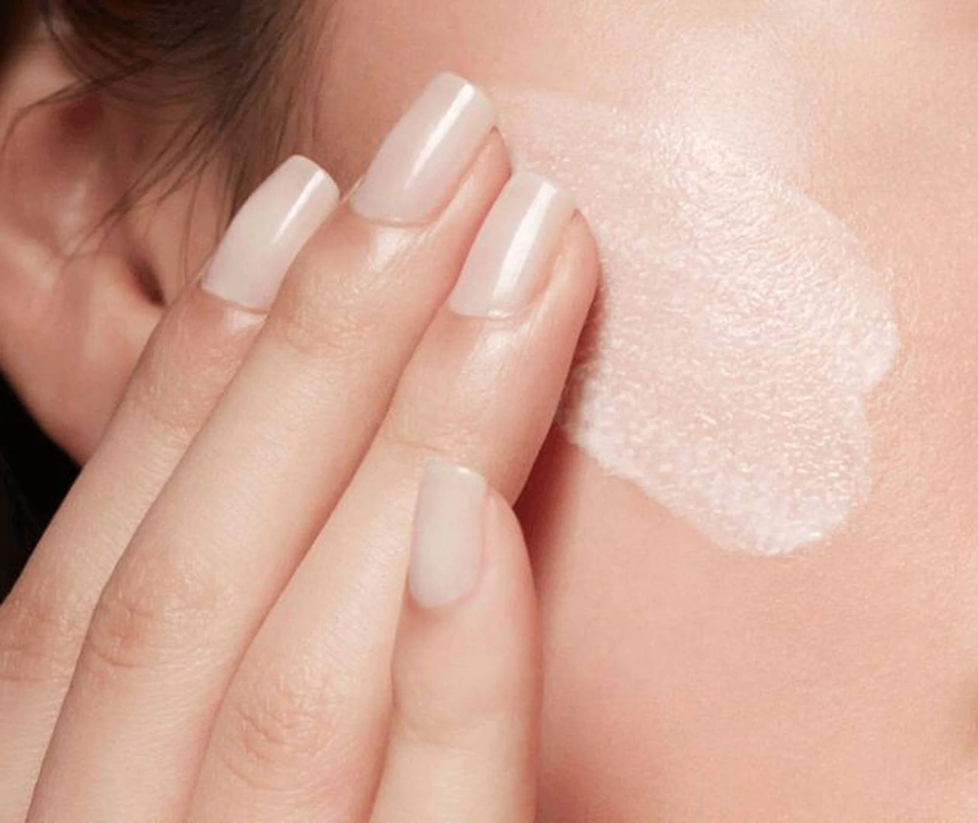 Close-up of a hand applying a white cream to skin