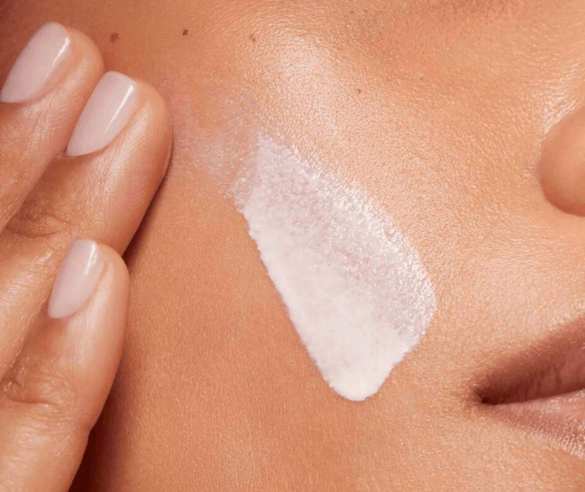 Close-up of a hand applying a white cream to skin