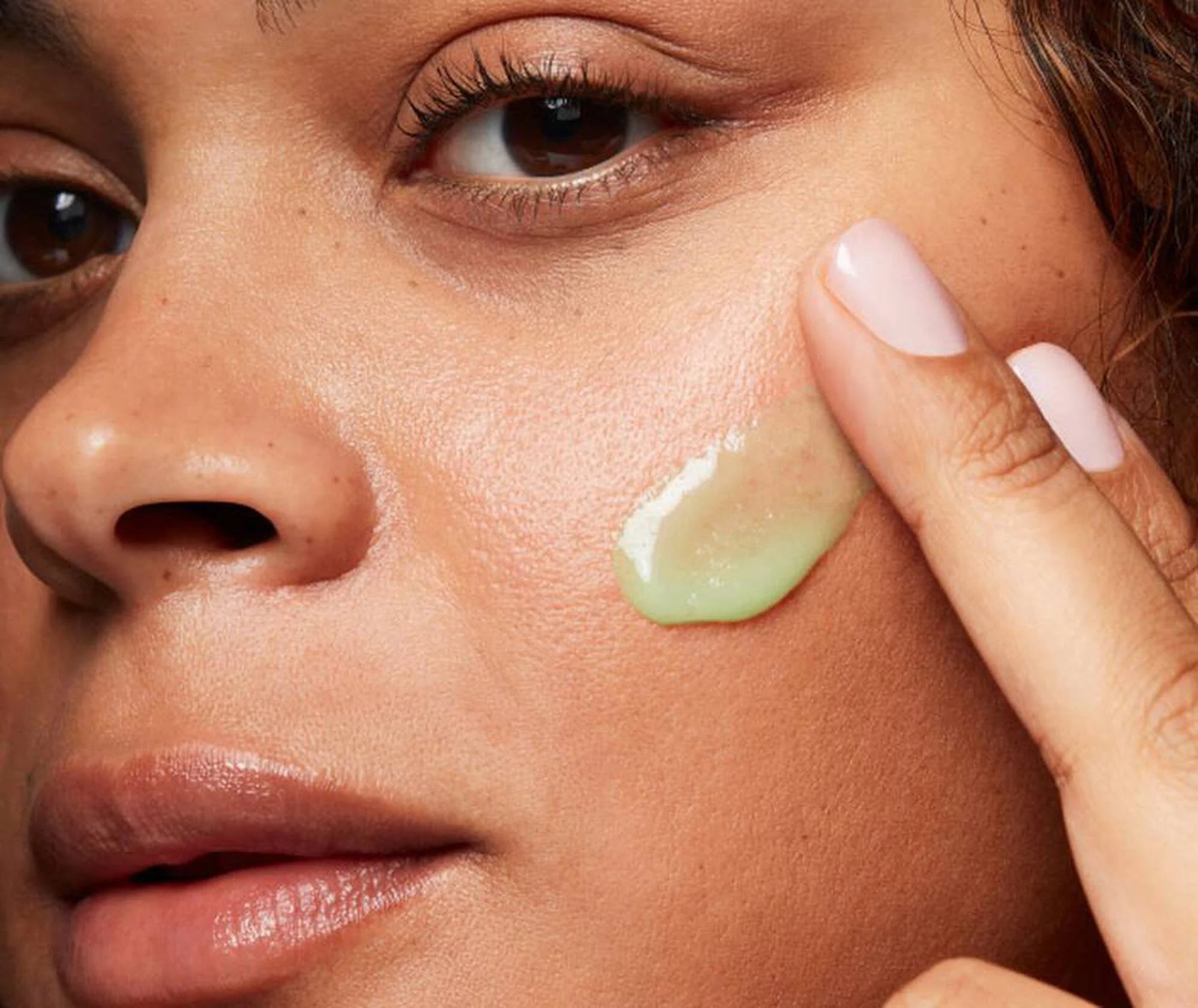 Close-up of a person applying green cream to their cheek.