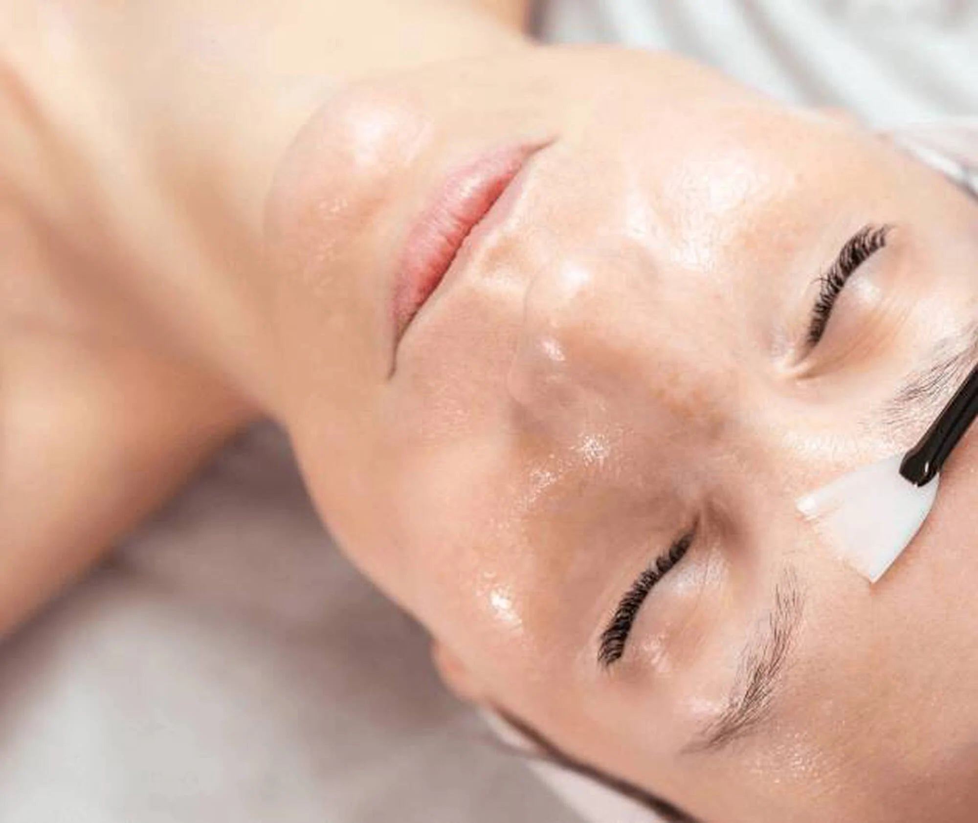 Close-up of a person receiving a facial treatment with a neutral background