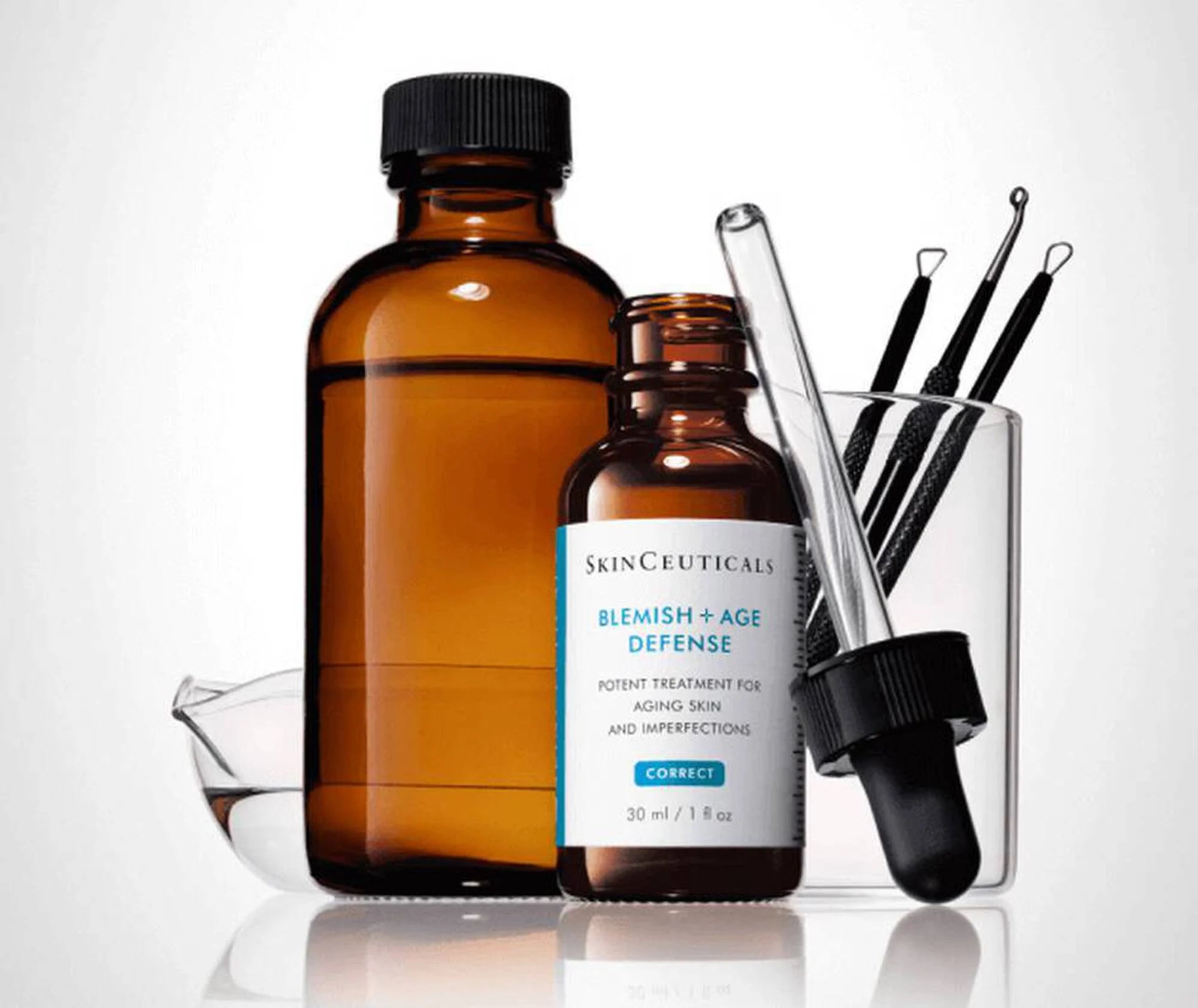 Two brown bottles with skincare products SkinCeuticals Blemish + Age Defense and tools on a white background