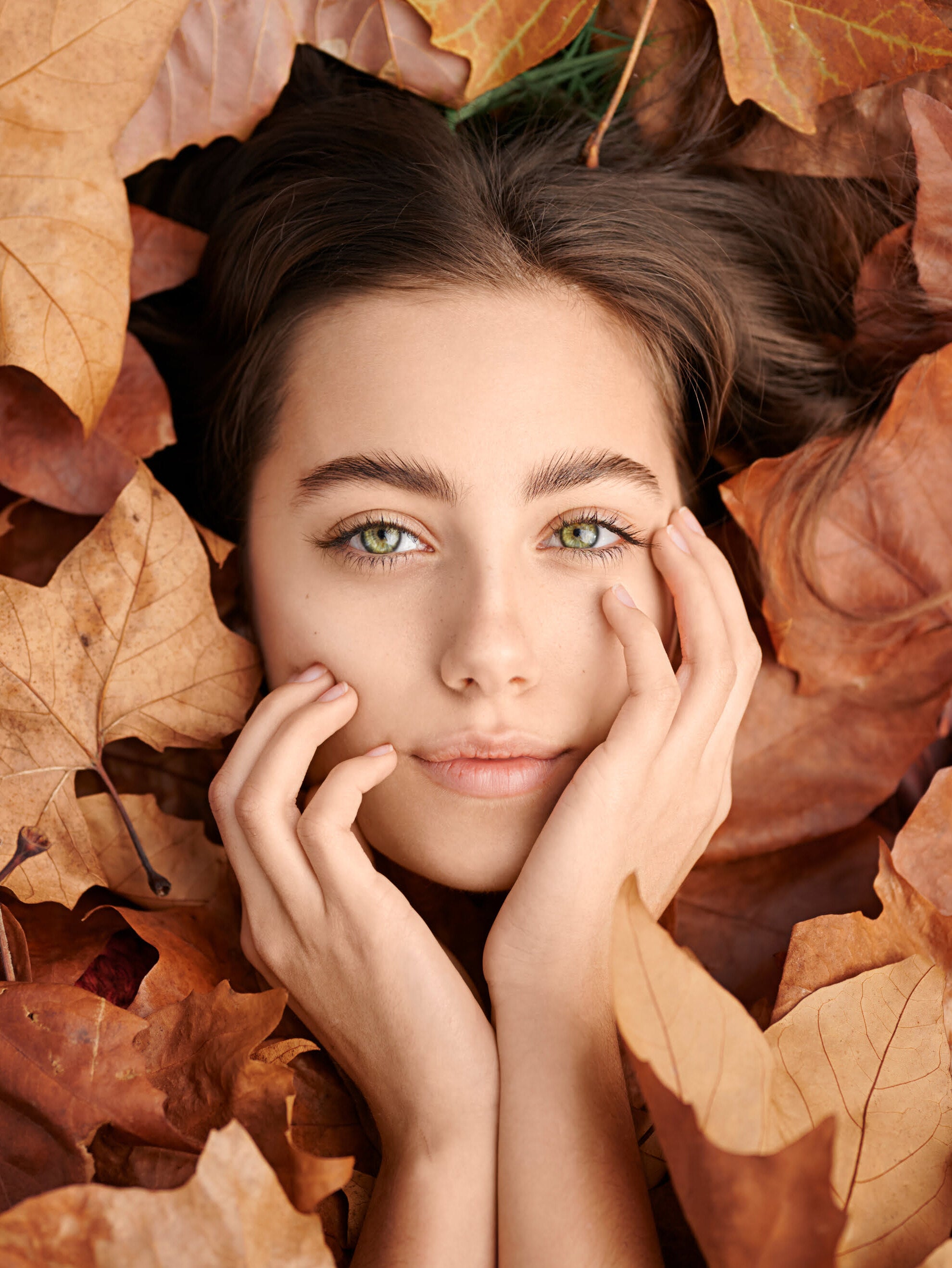 Woman lying among autumn leaves with a close-up of her face.